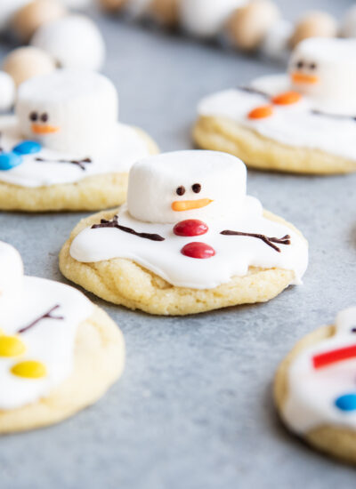 An above view of melted snowman cookies decorated with royal icing, mini m&ms, and marshmallows for their heads.