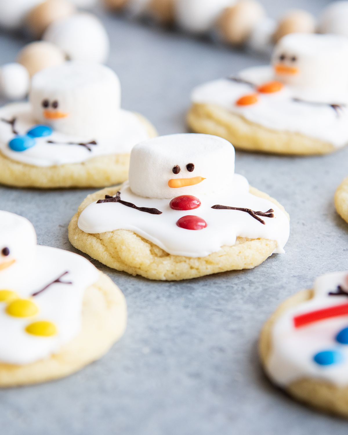 An above view of melted snowman cookies decorated with royal icing, mini m&ms, and marshmallows for their heads.