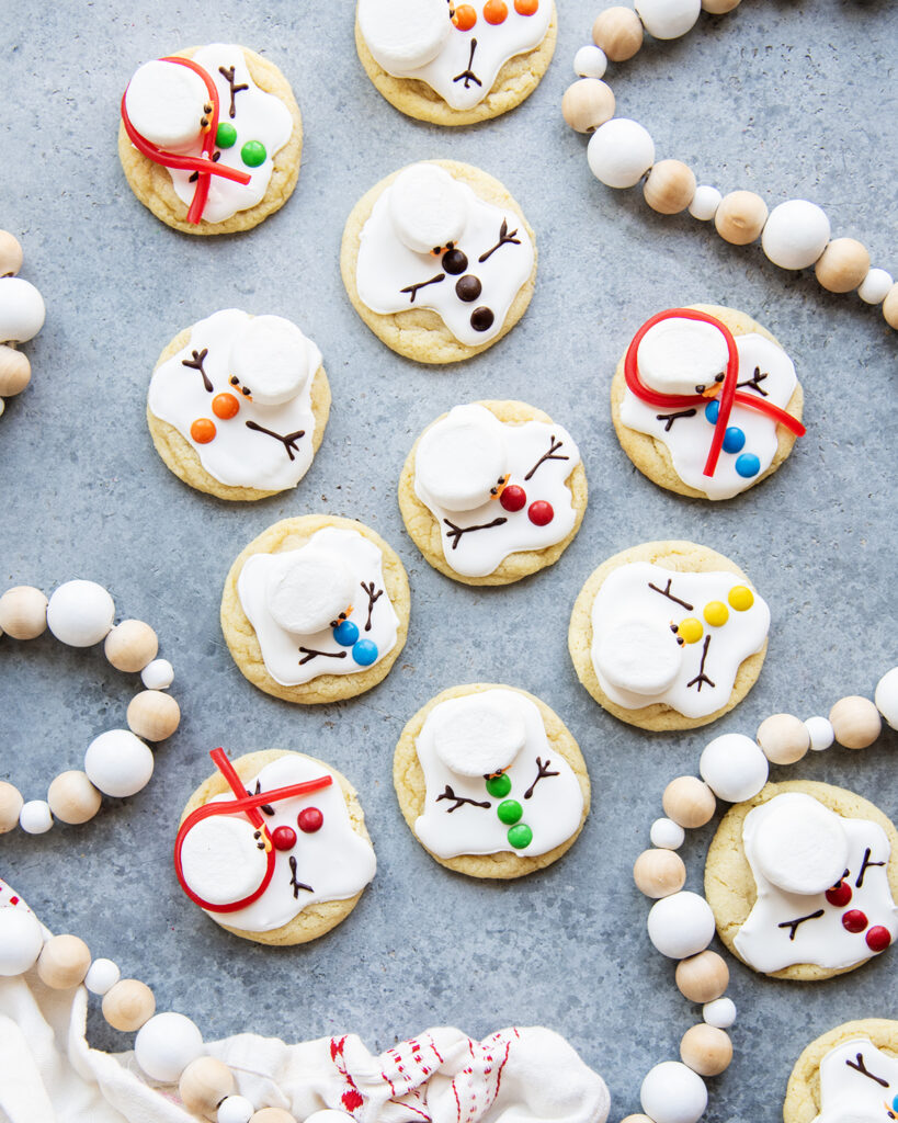 An above view of melted snowman cookies decorated with royal icing, mini m&ms, and marshmallows for their heads.