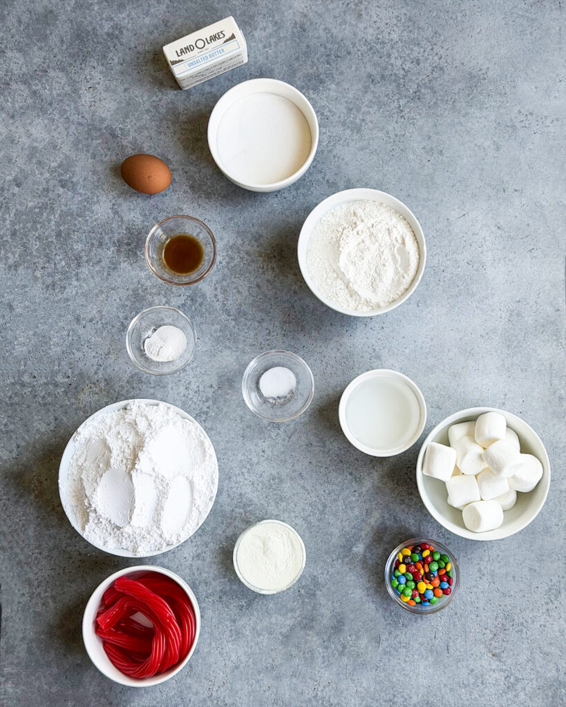 Small bowls of the ingredients needed to make melted snowman cookies, such as powdered sugar, flour, marshmallows, meringue powder, salt, an egg, etc.