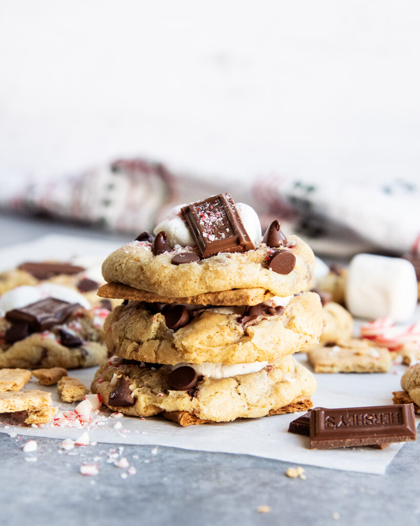 A stack of three peppermint smores cookies topped with a gooey marshmallow and chocolate piece.