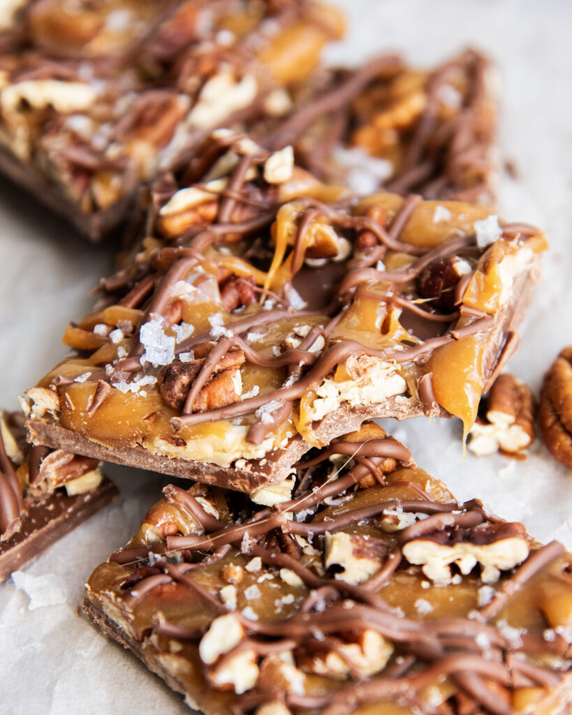 A pile of chocolate caramel pecan bark, the top piece has a bite out of it.