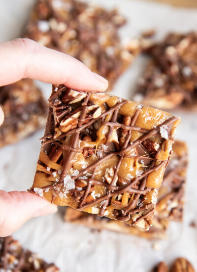 A hand holding a piece of chocolate caramel turtle bark.