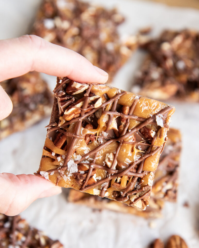A hand holding a piece of chocolate caramel turtle bark.