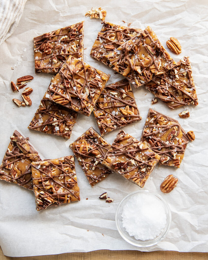 A pile of chocolate caramel pecan bark, its a chocolate bark topped with caramel, pecans and flakey sea salt.