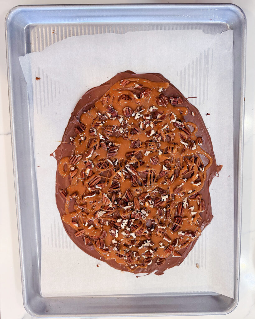 Chocolate spread on a piece of parchment paper topped with caramel and pecans.