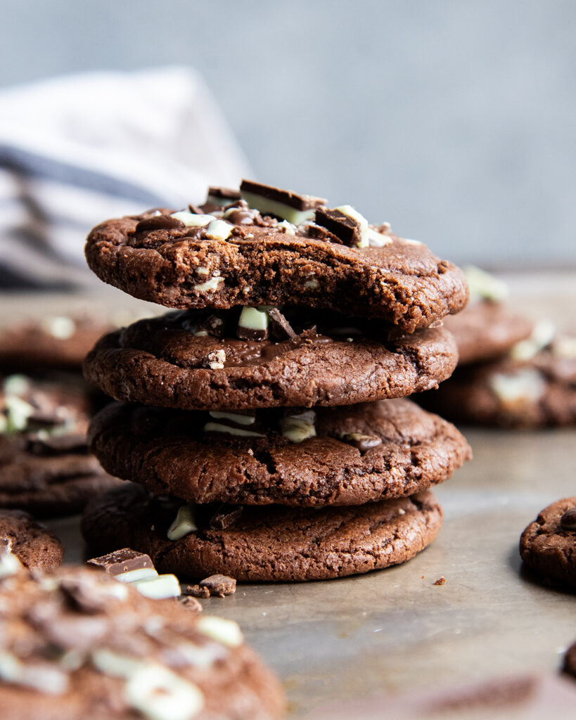 A stack of four chocolate mint cookies stuffed with Andes Mint chocolates, and the top cookie has a bite out of it.