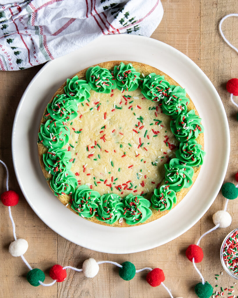 An above view of a Christmas Sugar Cookie Cake on a plate with Christmas sprinkles and green buttercream frosting on the sides.