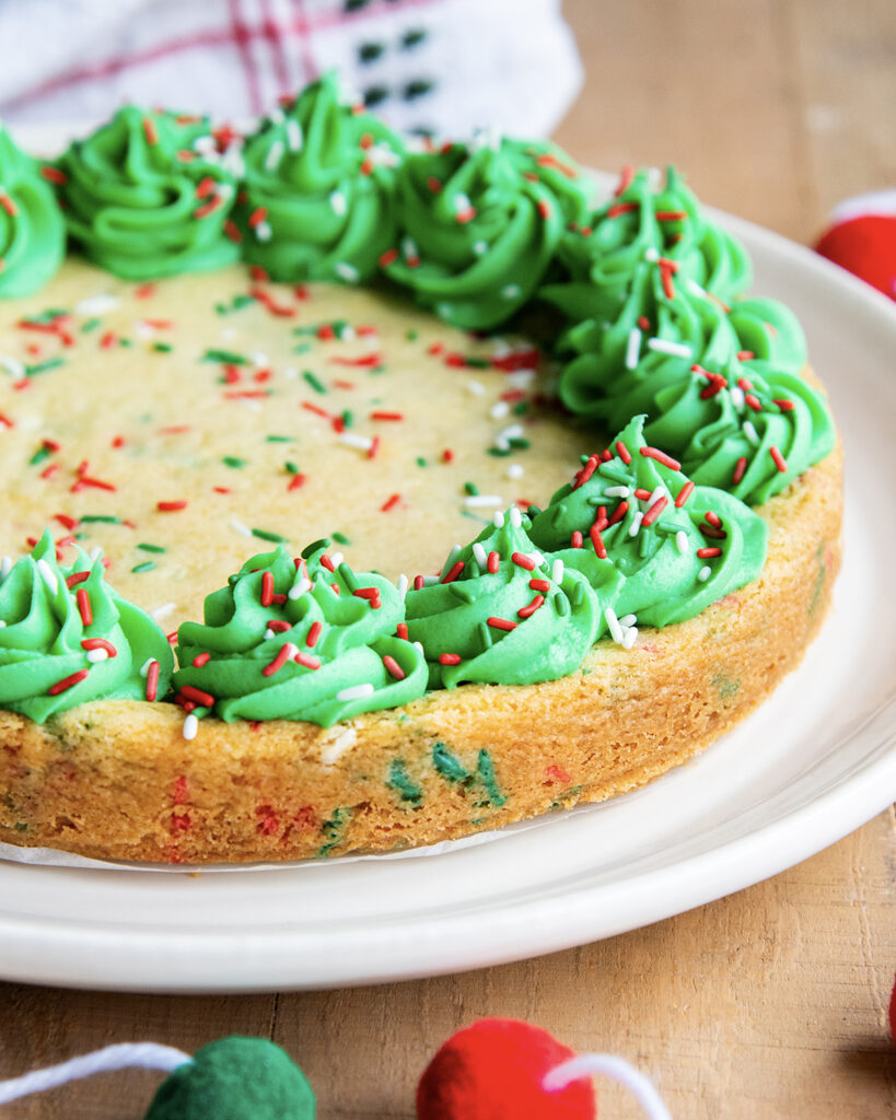 A Christmas Sugar Cookie Cake on a plate topped with green buttercream on the sides of the "cake".