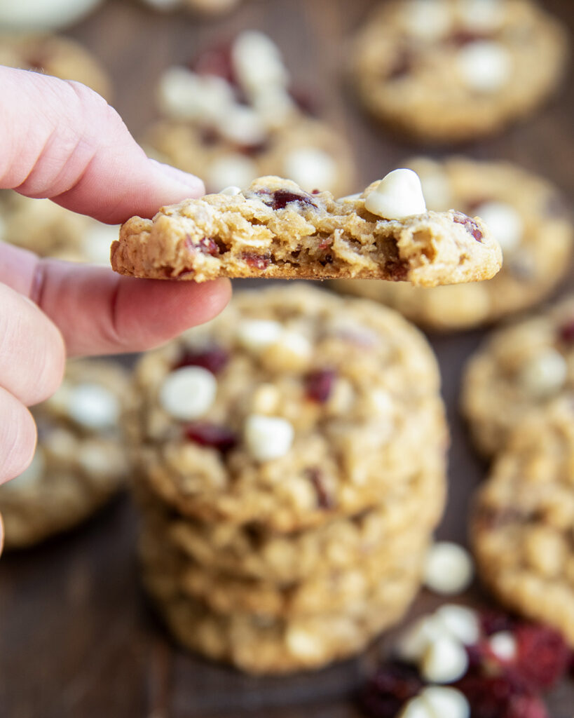 A hand holding an oatmeal cranberry white chocolate cookie with a bite out of it.