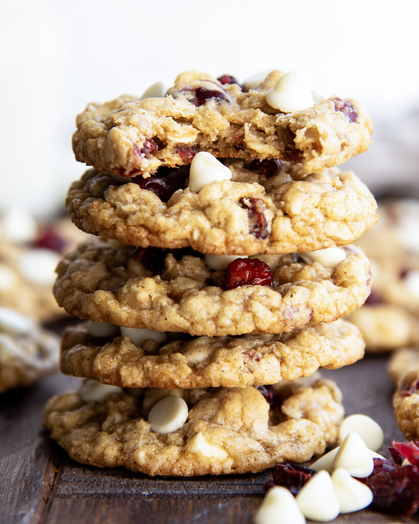 A stack of five oatmeal white chocolate and cranberry cookies, and the top cookie has a bite out of it.