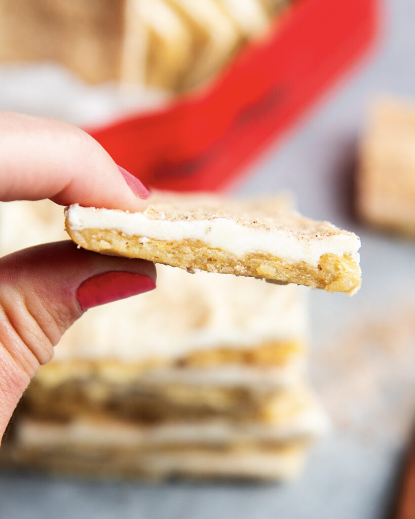 A piece of churro cracker toffee in a hand, with white chocolate and cinnamon sugar on top.