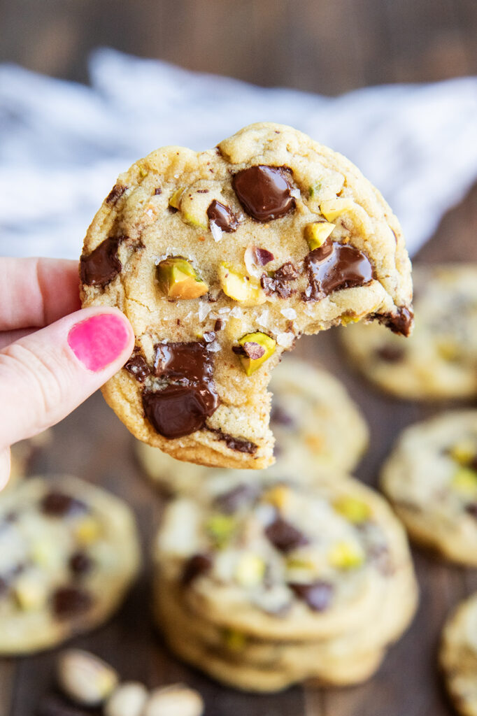 A hand holding a pistachio chocolate chip cookie with a bite out of it.