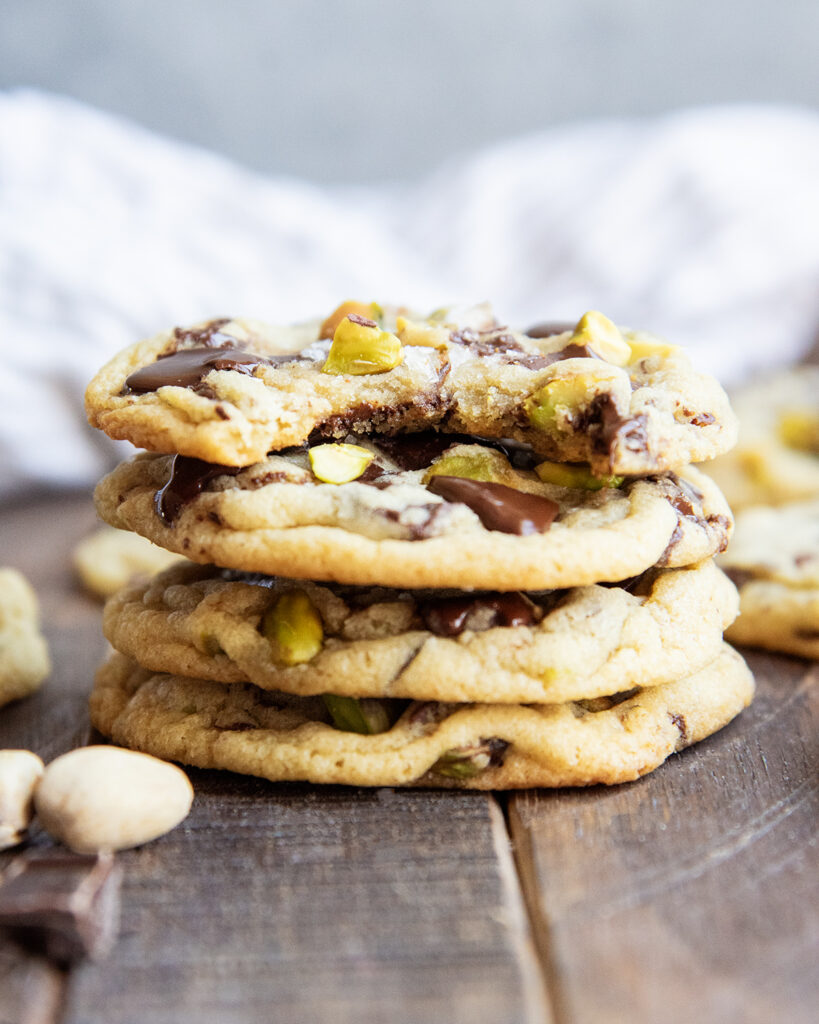 A stack of four pistachio chocolate chip cookies, and the top cookie has a bite out of it.