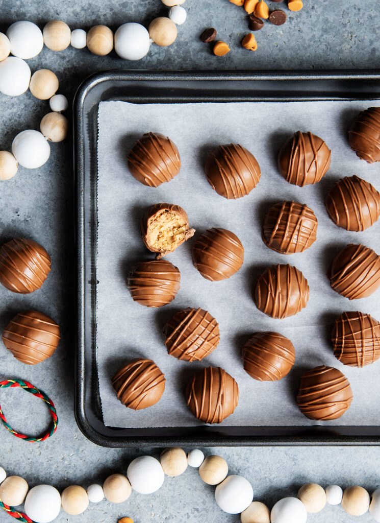 A metal baking tray topped with chocolate scotcheroo balls, one is bit open showing the peanut butter center.
