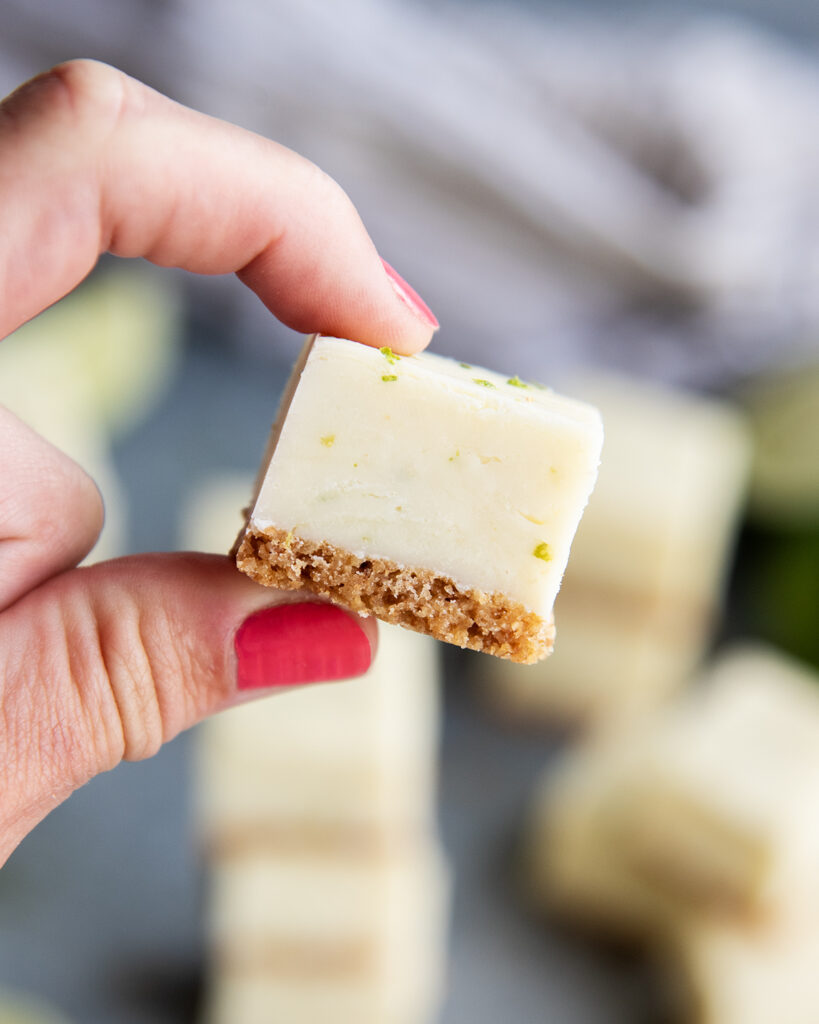 A hand holding a piece of key lime pie fudge with a graham cracker crust.