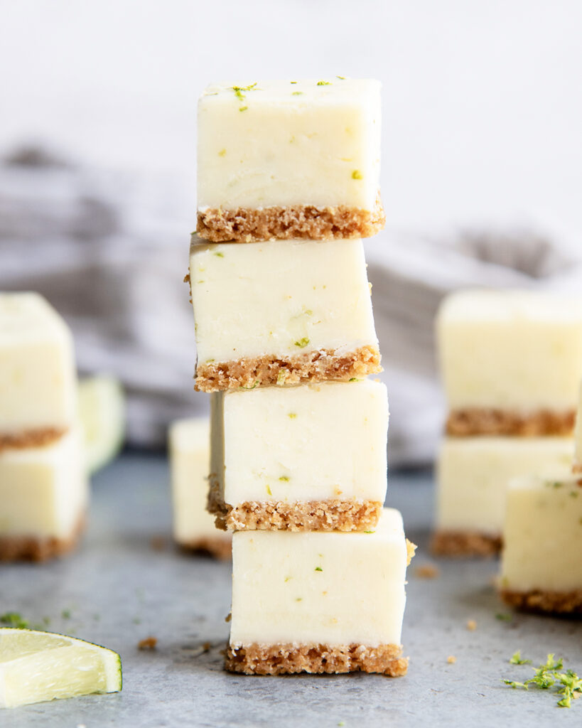 A stack of four pieces of key lime pie fudge, with a graham cracker crust and lime zest pieces in the fudge.