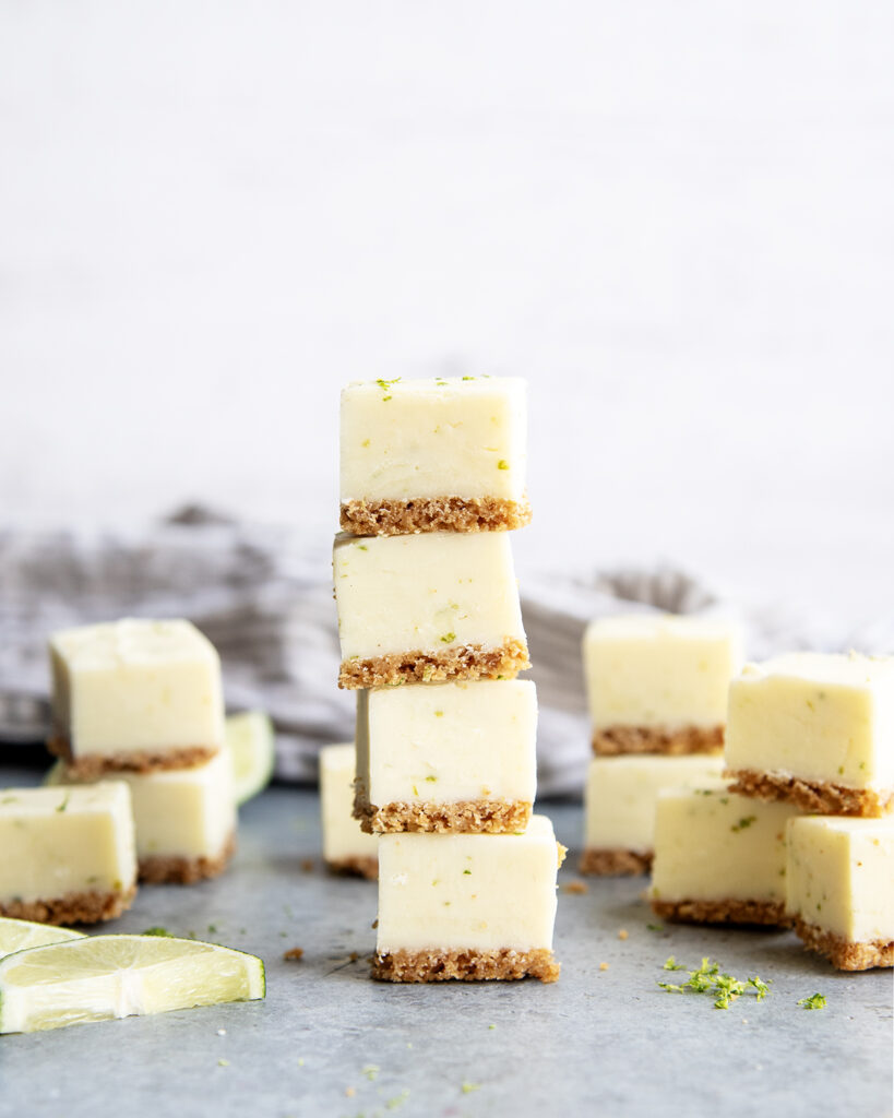 A stack of four pieces of key lime pie fudge, with a graham cracker crust and lime zest pieces in the fudge.