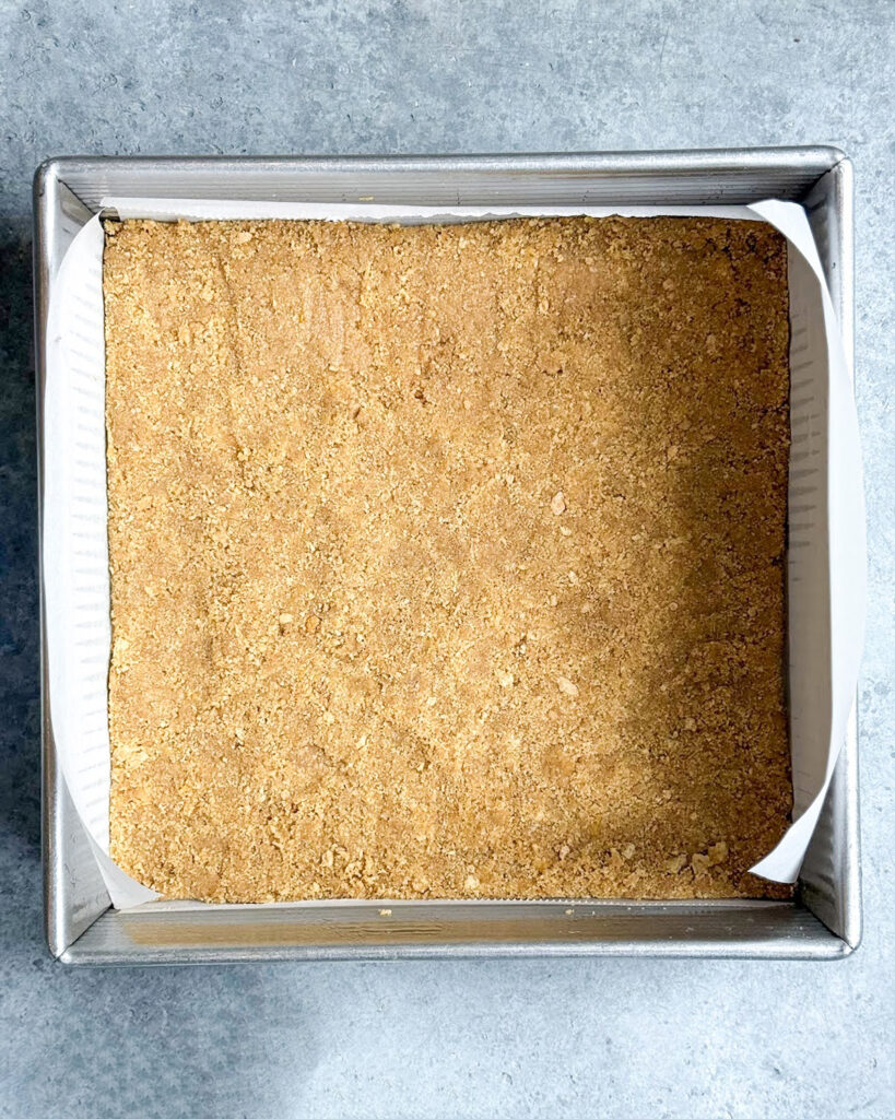 A graham cracker crust in a square baking pan.