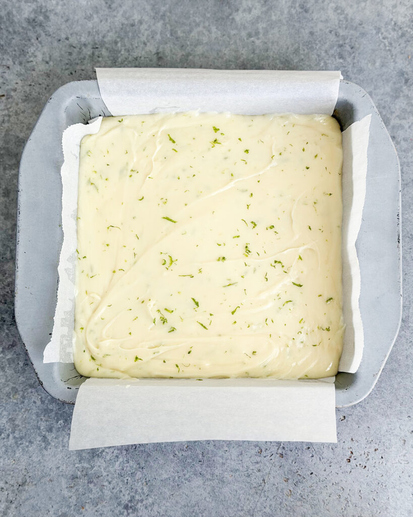 An above view of a pan of white chocolate fudge with lime zest pieces.