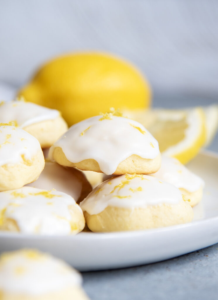 A close up of Italian Lemon Ricotta Cookies topped with white icing and lemon zest on a white plate.