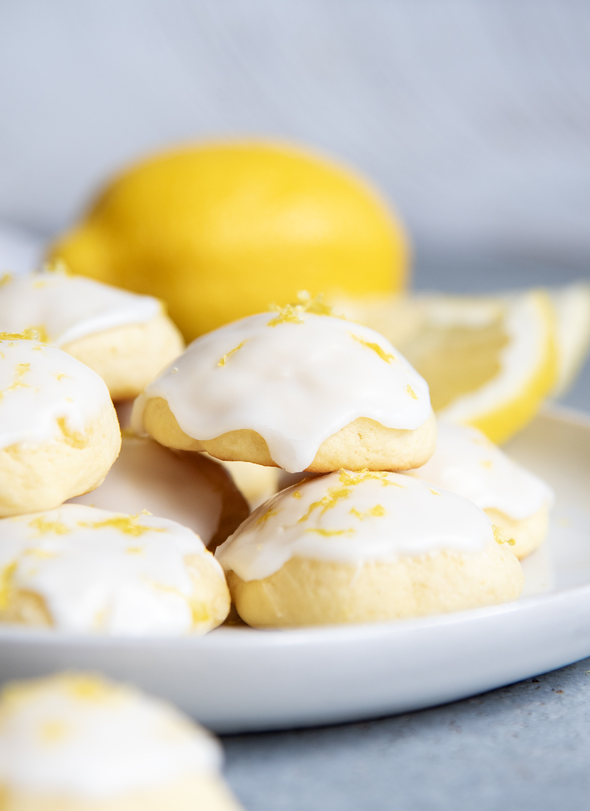 A close up of Italian Lemon Ricotta Cookies topped with white icing and lemon zest on a white plate.