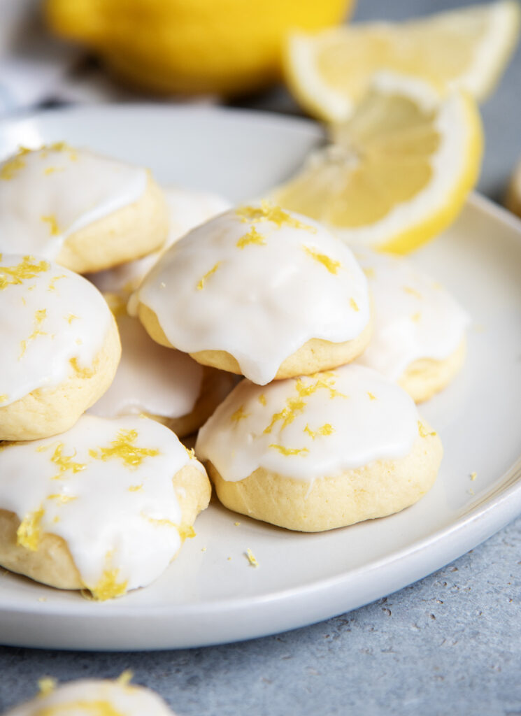 A close up of Italian Lemon Ricotta Cookies topped with white icing and lemon zest on a white plate.