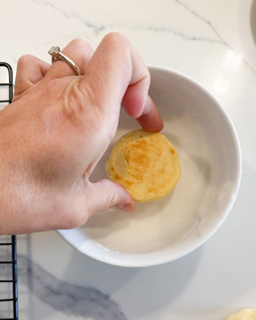 Dipping a lemon ricotta cookie into a bowl of icing.