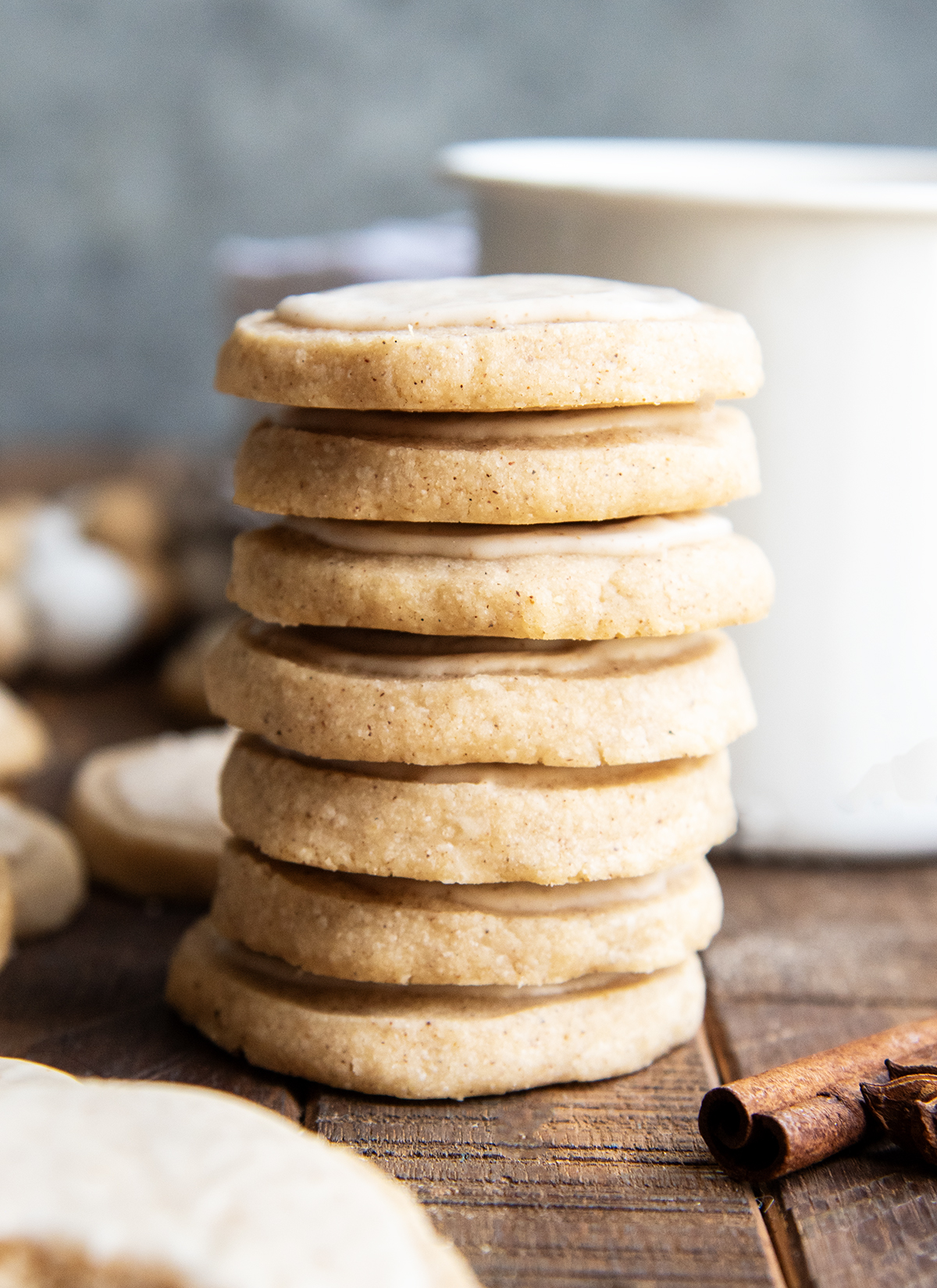 A stack of several shortbread cookies topped with icing and next to a mug of chai.