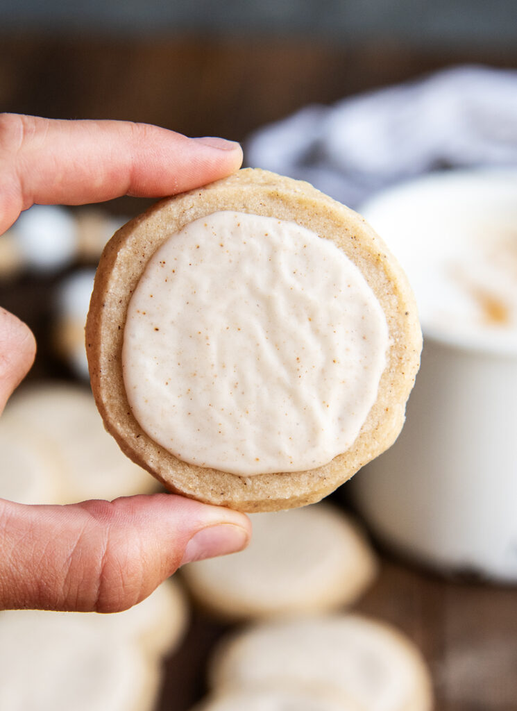 A hand holding a round iced chai tea shortbread cookie.