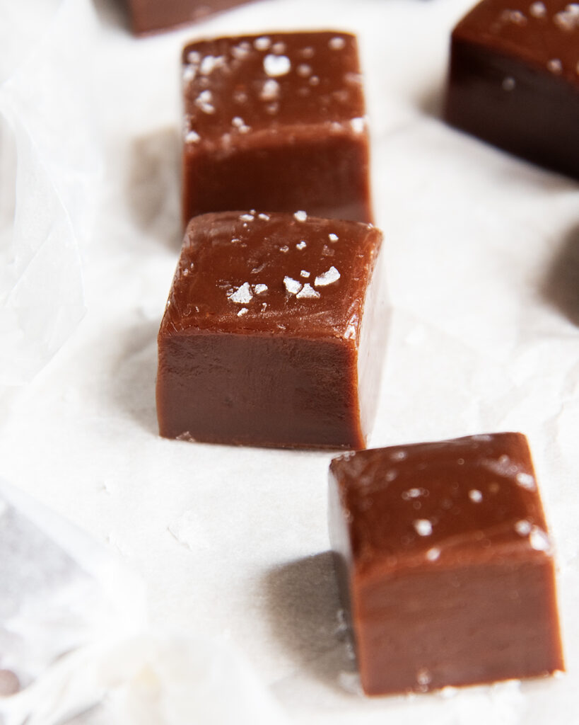 A close up of three chewy chocolate caramels with sea salt on top. 