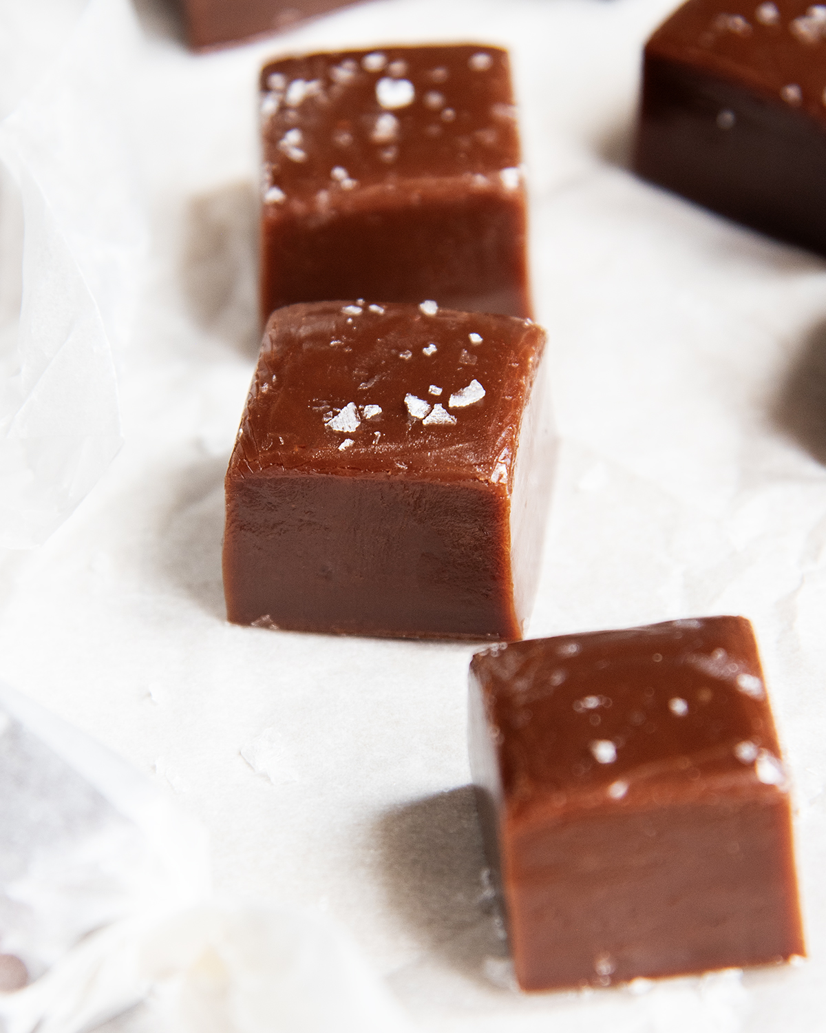 A close up of three chewy chocolate caramels with sea salt on top.