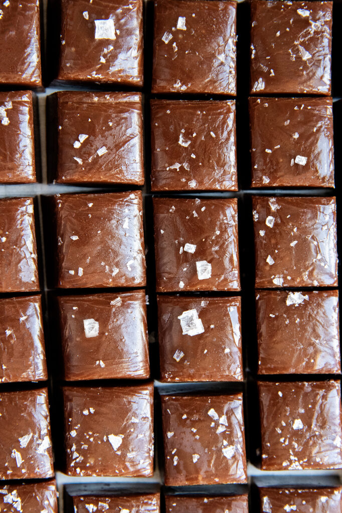 An above view of rows of chocolate caramels topped with flakey sea salt.