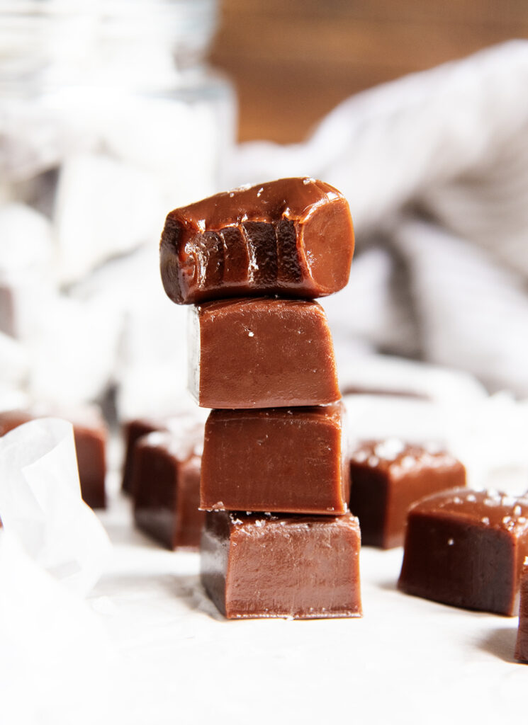 A stack of four squares of chocolate flavored caramel. The top has a bite out of it.