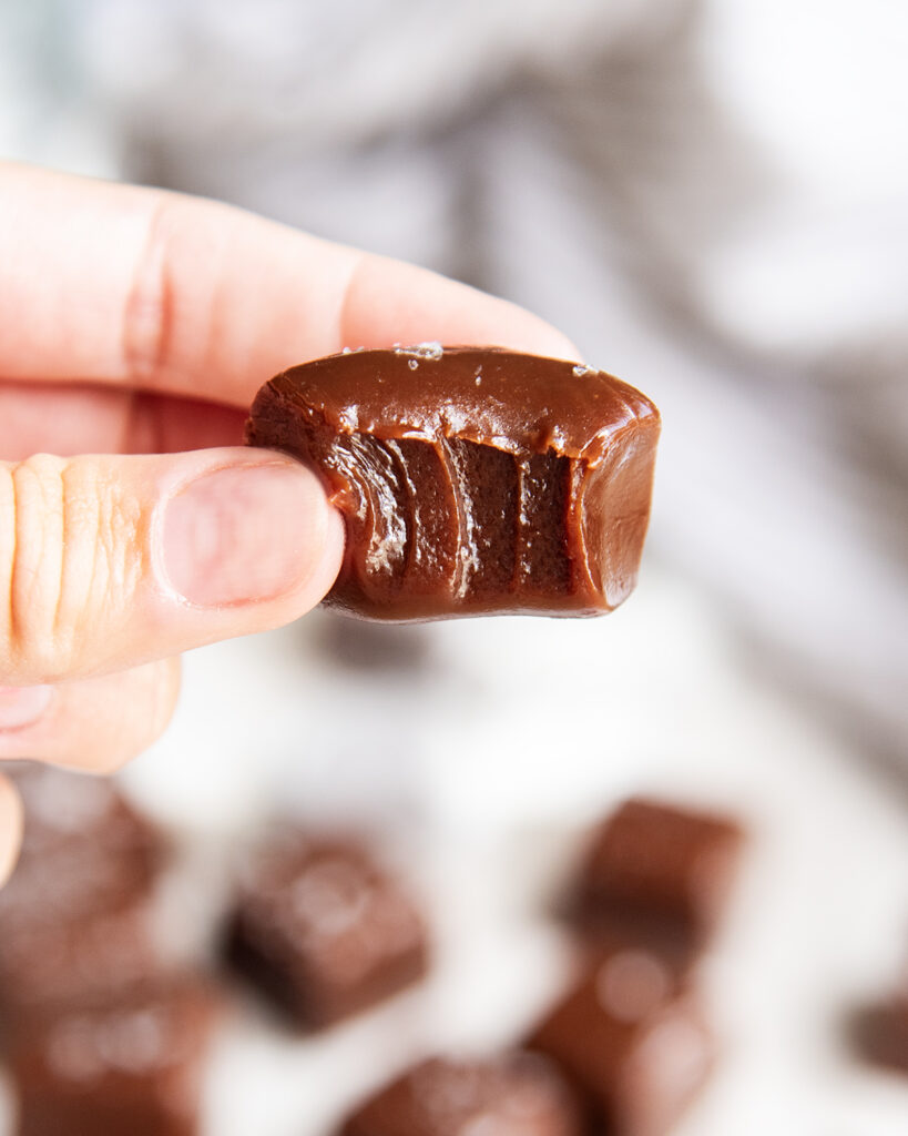 A hand holding a chewy chocolate caramel with a bite out of it.