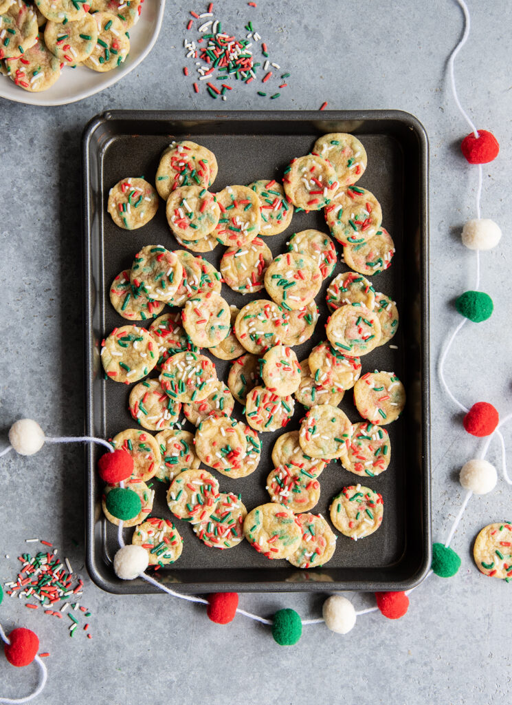 An above view of a cookie pan with lots of mini christmas sprinkle sugar cookies on it.