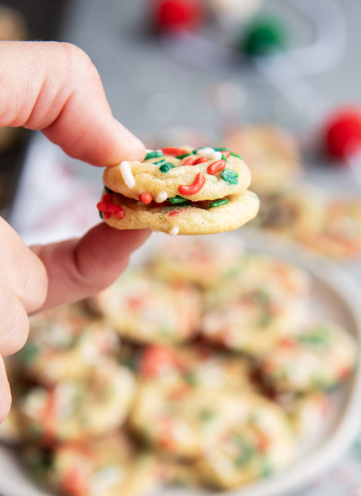 A hand holding two mini sugar christmas funfetti sugar cookies.