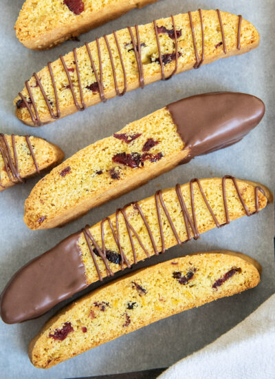 A cookie pan topped with cranberry orange biscotti, some are dipped half way in chocolate, and some are drizzled with chocolate.