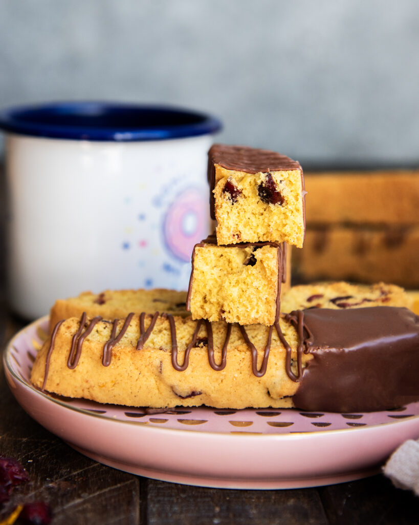 A stack of cranberry orange biscotti pieces and two of them are broken in half showing the center of the biscotti.