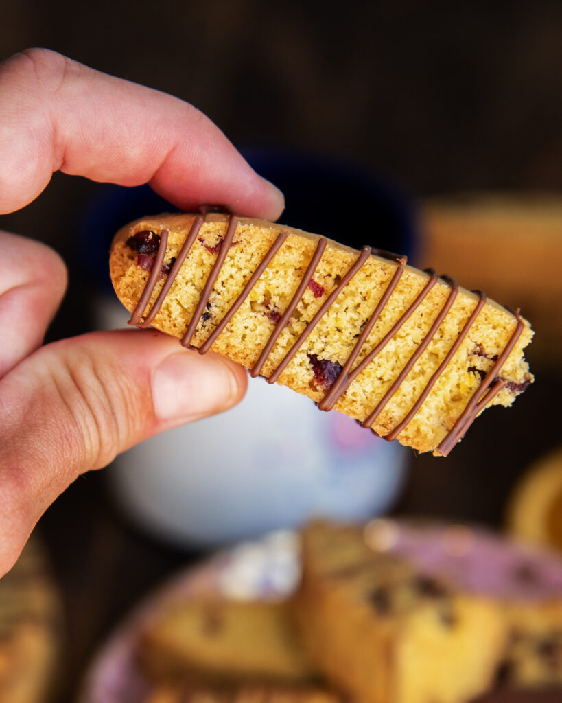 Half a biscotti drizzled with chocolate held in a hand.