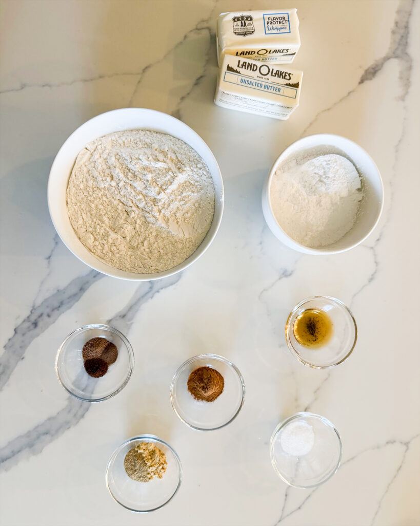 Small bowls of the ingredients needed to make vanilla chai shortbread cookies, there are bowls of flour, powdered sugar, spices, and butter. 