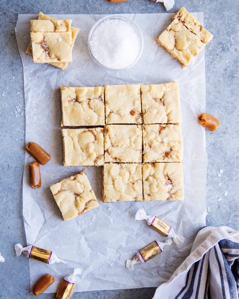 An above view of rows of caramel shortbread cookie bars topped with flakey sea salt.