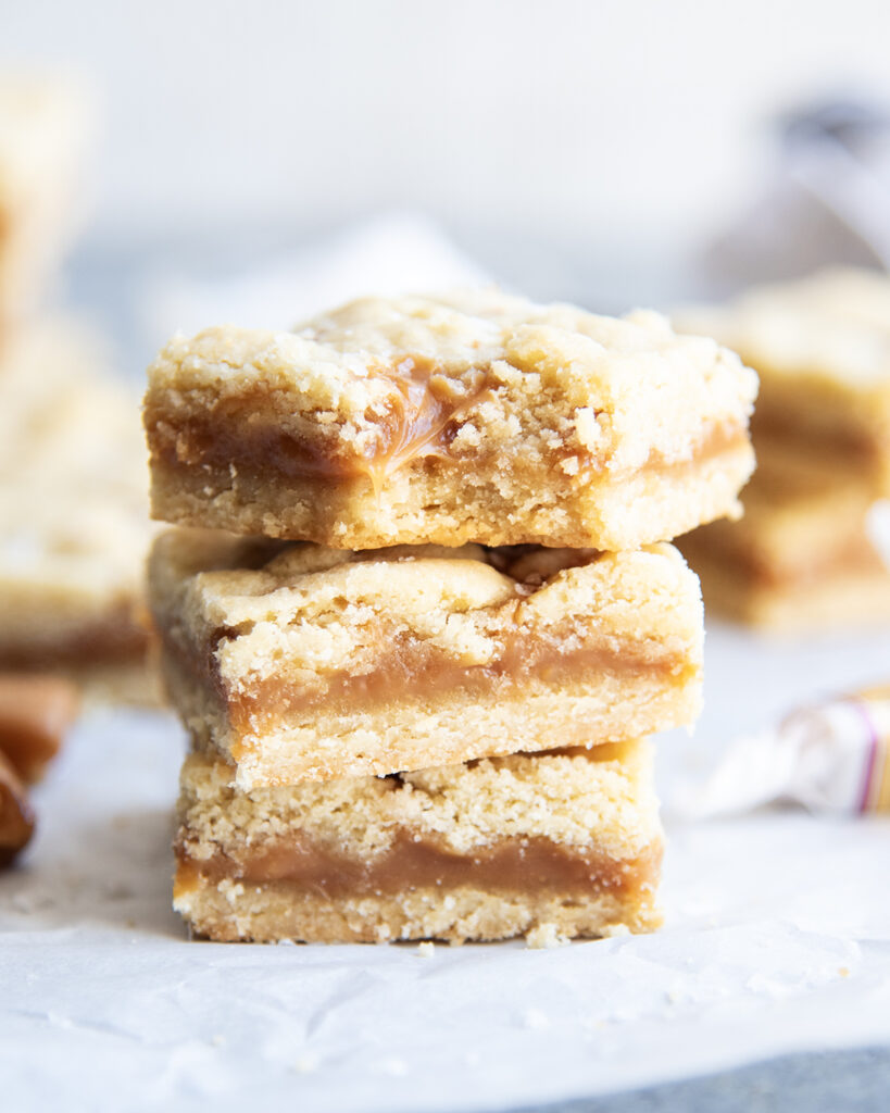 A stack of three shortbread cookie bars with a layer of caramel in the middle.