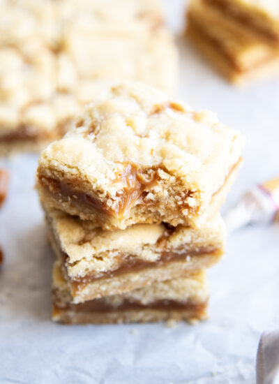 A stack of caramel shortbread cookie bars, and the top bar has a bite out of it.