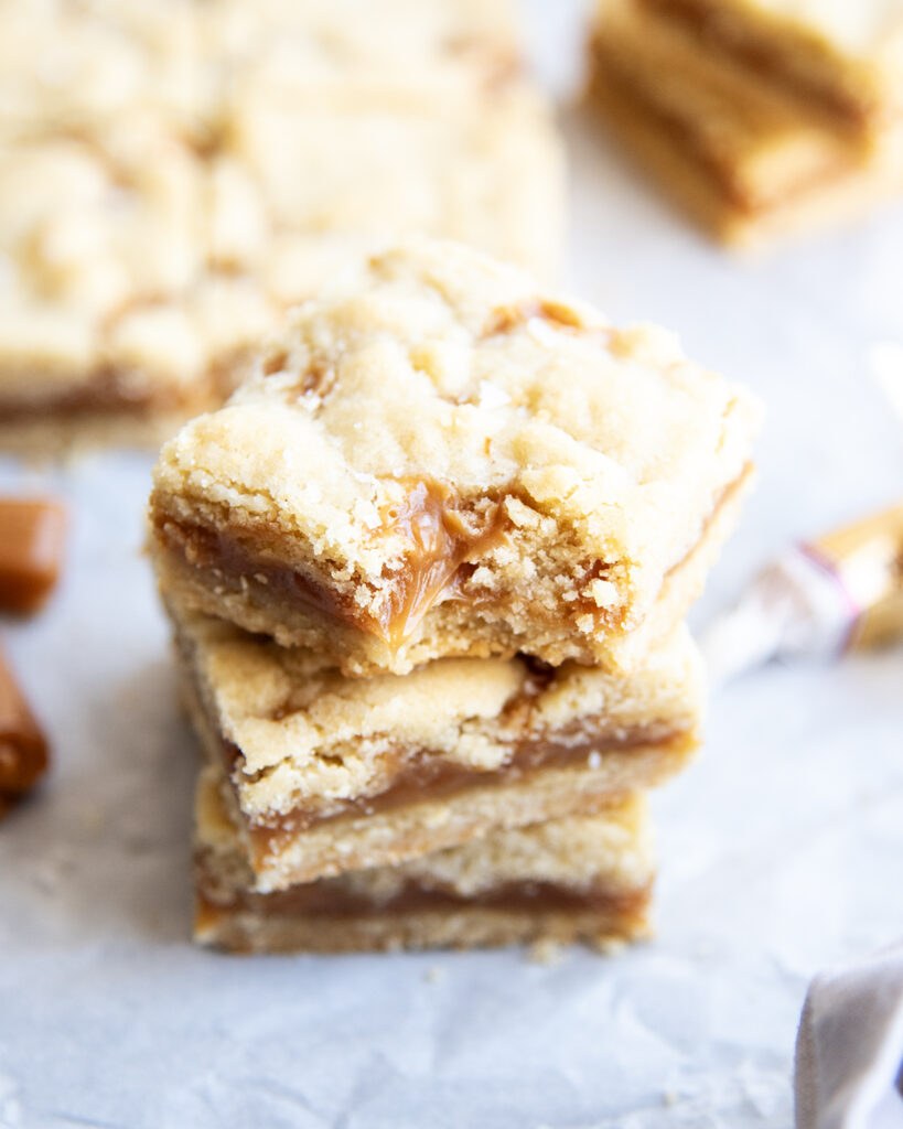 A stack of caramel shortbread cookie bars, and the top bar has a bite out of it.