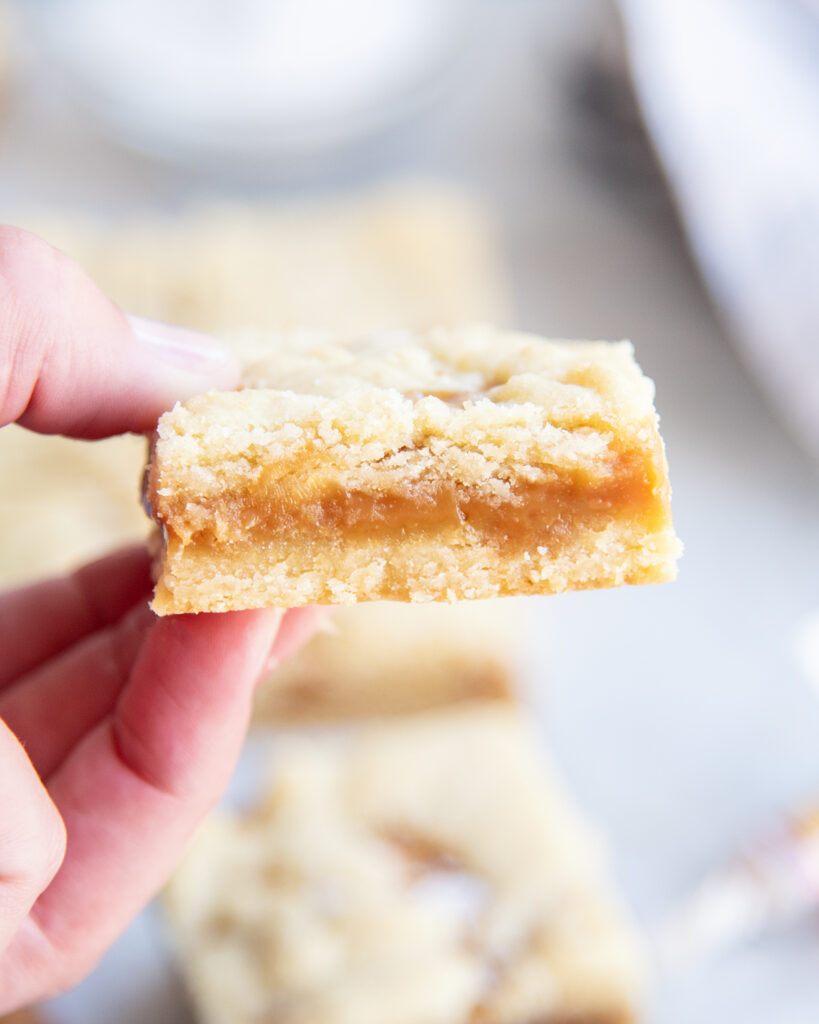 A hand holding a caramel filled shortbread cookie bar.