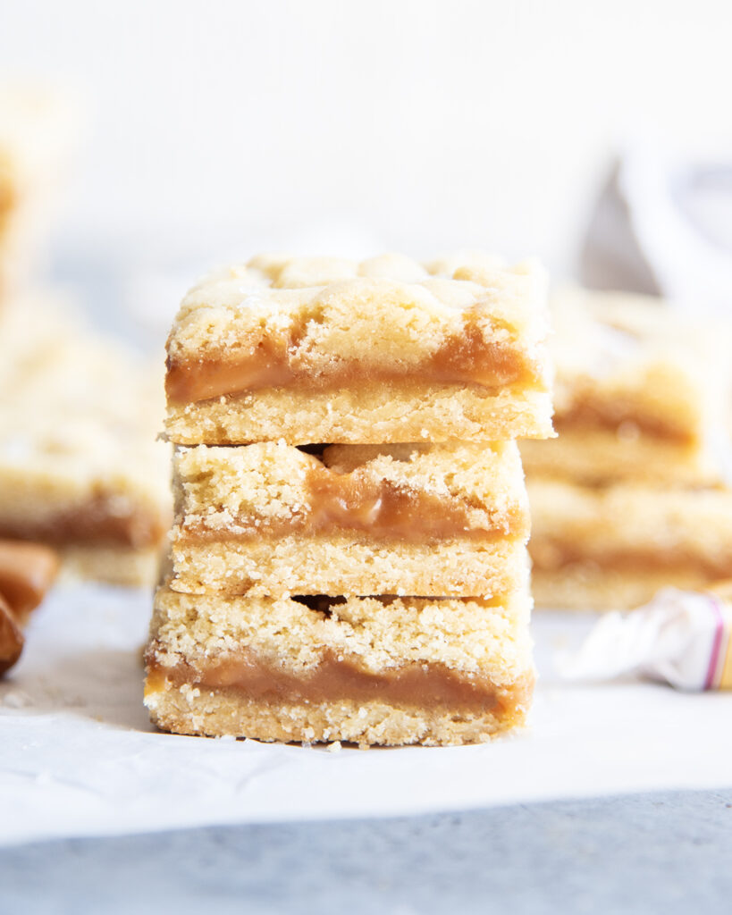 A stack of three caramel shortbread cookie bars with a gooey layer of caramel in the middle.