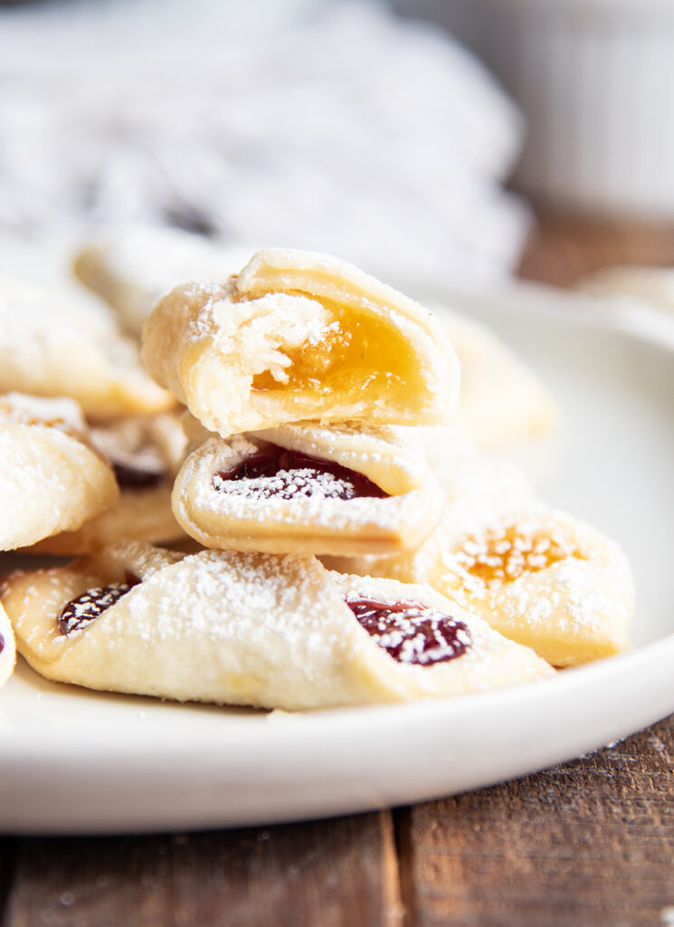 A stack of kolacky cookie on a plate, the top cookie has a bite out of it.