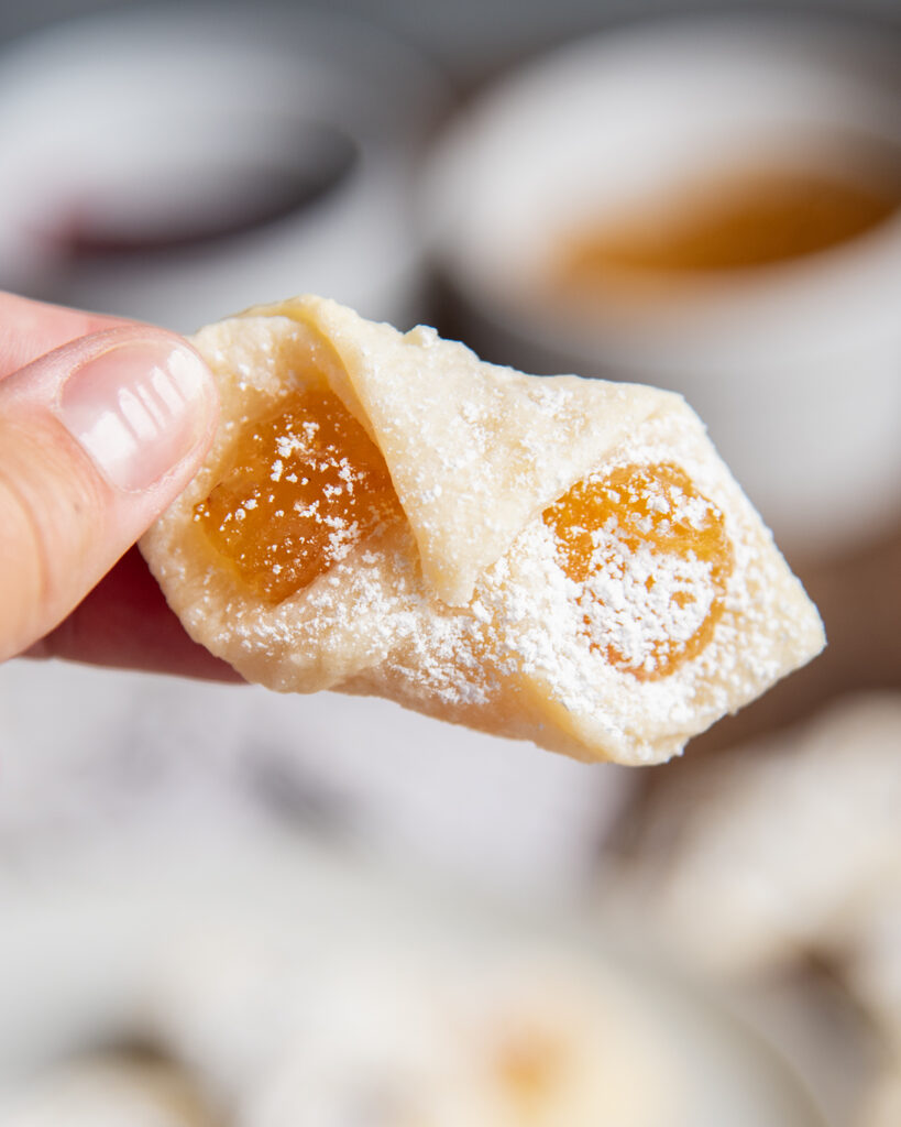 A hand holding a kolacky cookie filled with apricot jam.