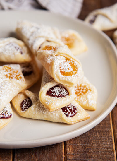 A pile of pastry cookies filled with raspberry and apricot jam, topped with powdered sugar.